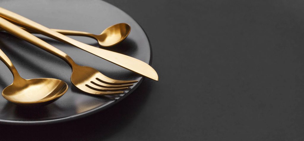 Schönes Goldbesteck - Gabel, Messer, Löffel, Dessertlöffel auf schwarzem Teller auf schwarzem Hintergrund